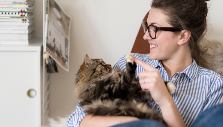 Eine Frau sitzt mit ihrer Katze auf dem Schoß und berührt ihre Pfote mit einem Finger