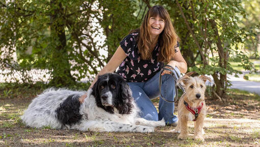 Tiertrainerin der Kompetenzstelle 'A G’spia fürs Tier' sitzt mit 2 Hunden auf einer Wiese.